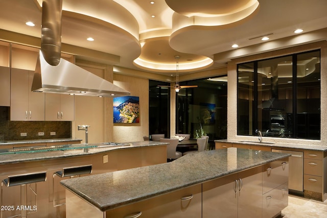 kitchen with sink, stone countertops, a tray ceiling, island range hood, and a kitchen island