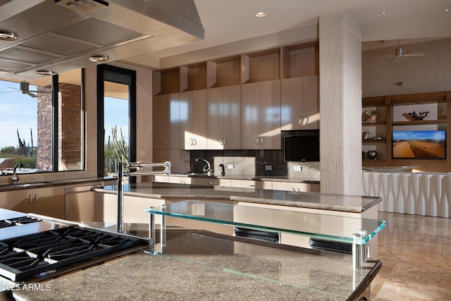 kitchen featuring backsplash, dark stone counters, ventilation hood, gas stovetop, and sink