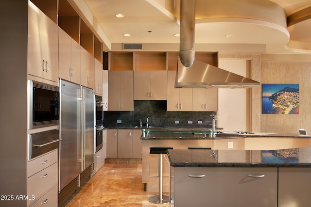 kitchen featuring a kitchen bar, appliances with stainless steel finishes, sink, a center island with sink, and dark stone countertops