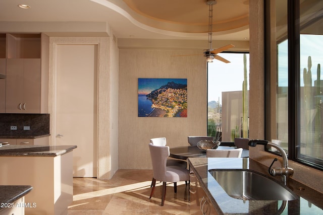 dining area with a raised ceiling, ceiling fan, and sink