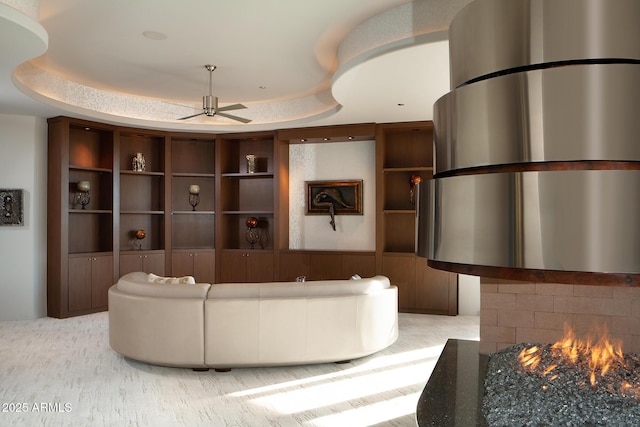 living room with ceiling fan, built in shelves, and a tray ceiling