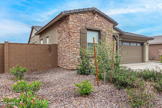 view of front of home featuring a garage, stone siding, concrete driveway, and fence