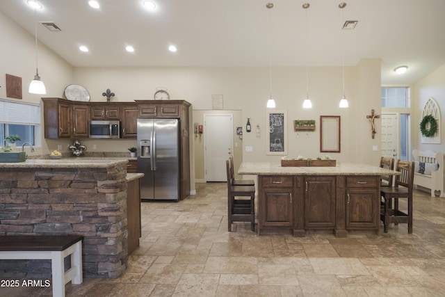 kitchen with appliances with stainless steel finishes, a breakfast bar area, stone tile flooring, dark brown cabinets, and recessed lighting