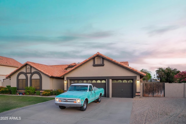 view of front of property with driveway, a garage, stucco siding, fence, and a gate