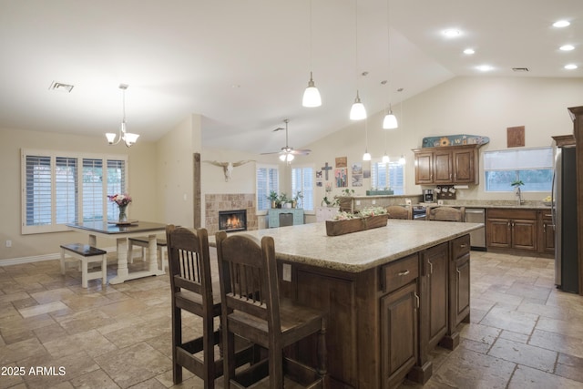 kitchen with stainless steel appliances, stone tile floors, high vaulted ceiling, a kitchen island, and a tile fireplace