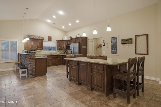 kitchen featuring appliances with stainless steel finishes, high vaulted ceiling, a breakfast bar area, stone tile flooring, and baseboards