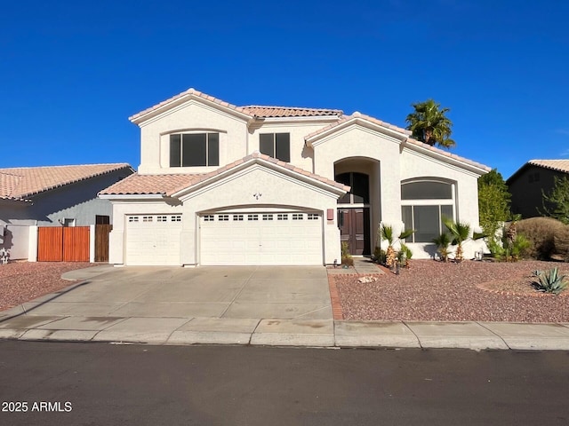 mediterranean / spanish house with a tiled roof, fence, concrete driveway, and stucco siding