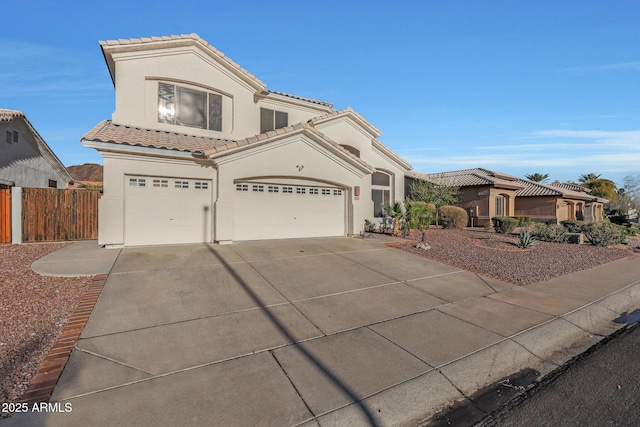 mediterranean / spanish house with a garage, fence, concrete driveway, a tiled roof, and stucco siding