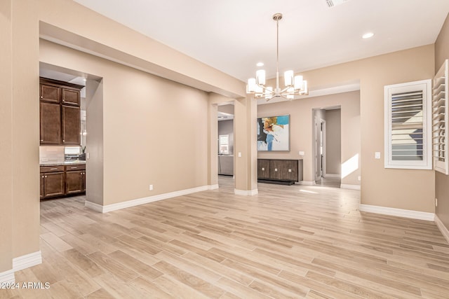 unfurnished living room with light wood-type flooring and a notable chandelier