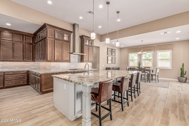 kitchen featuring pendant lighting, wall chimney exhaust hood, light wood-type flooring, and a large island with sink