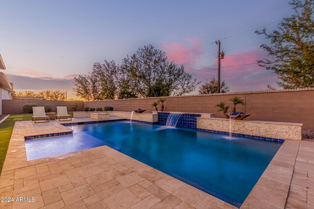 pool at dusk with a patio area and pool water feature