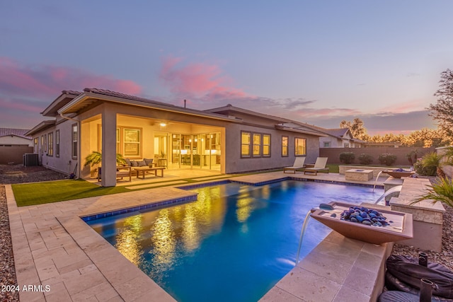 pool at dusk with an outdoor living space, pool water feature, central AC, and a patio area