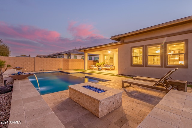 pool at dusk with a patio area, pool water feature, and an outdoor living space with a fire pit