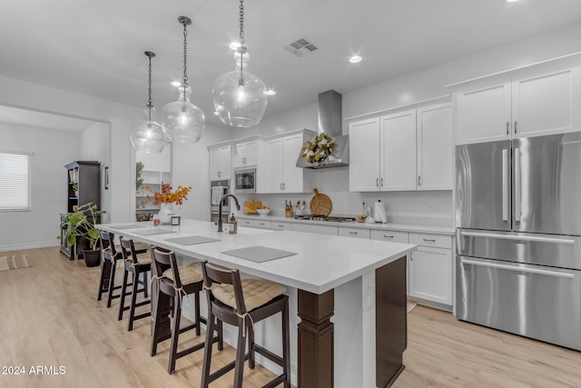 kitchen featuring visible vents, an island with sink, appliances with stainless steel finishes, white cabinetry, and wall chimney range hood