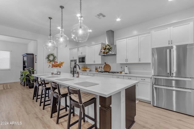 kitchen with visible vents, a kitchen island with sink, freestanding refrigerator, wall chimney exhaust hood, and built in microwave