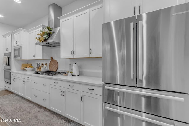 kitchen with stainless steel appliances, light stone countertops, wall chimney exhaust hood, and white cabinetry