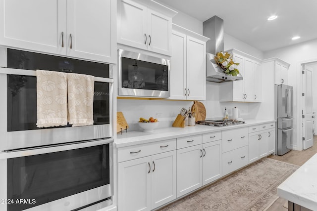 kitchen with recessed lighting, appliances with stainless steel finishes, white cabinetry, and wall chimney exhaust hood