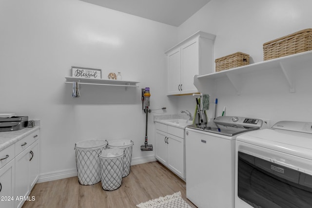 clothes washing area with baseboards, washing machine and dryer, light wood-style floors, cabinet space, and a sink