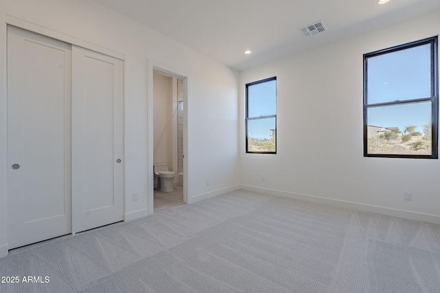 unfurnished bedroom with ensuite bath, a closet, and light carpet