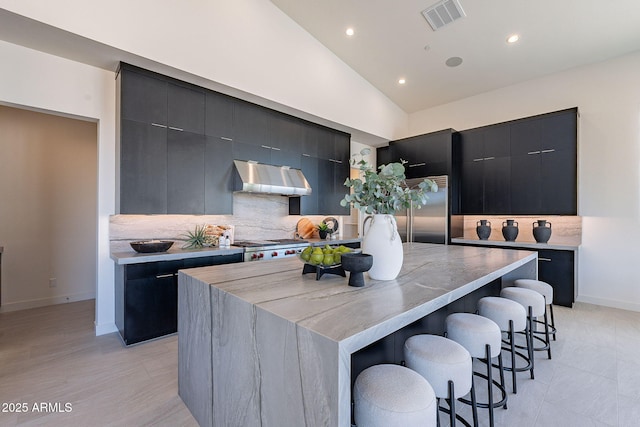 kitchen featuring a spacious island, a breakfast bar, vaulted ceiling, built in fridge, and decorative backsplash