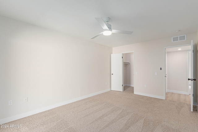 unfurnished bedroom with a spacious closet, light carpet, a closet, and ceiling fan