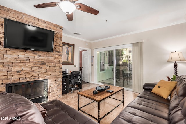 tiled living room with ceiling fan, a stone fireplace, and crown molding