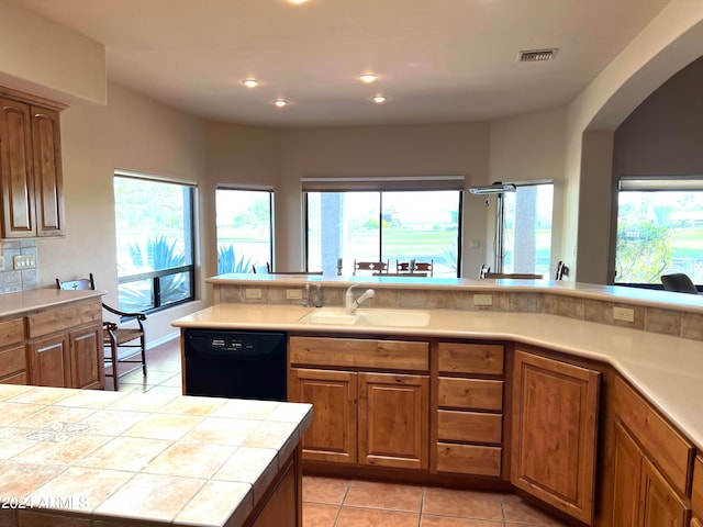 kitchen with black dishwasher, sink, light tile patterned floors, and tile countertops