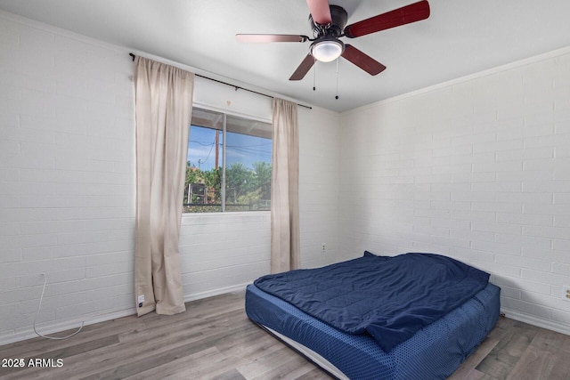 bedroom featuring ceiling fan, brick wall, and wood finished floors