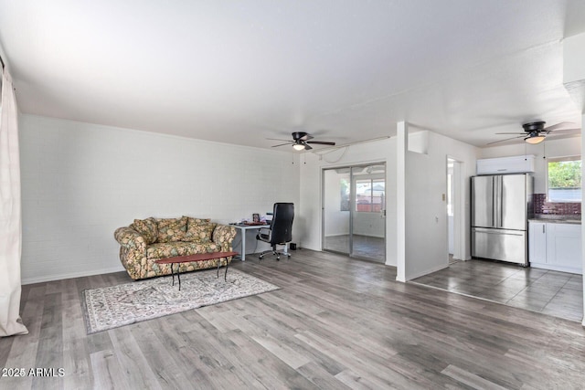 unfurnished living room with a ceiling fan, brick wall, and wood finished floors