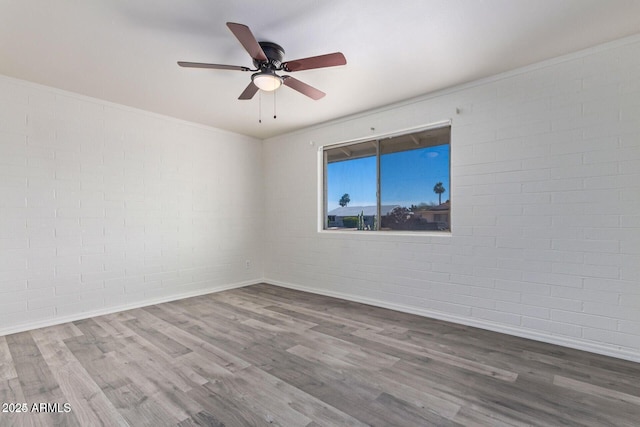 unfurnished room featuring baseboards, brick wall, ceiling fan, ornamental molding, and wood finished floors