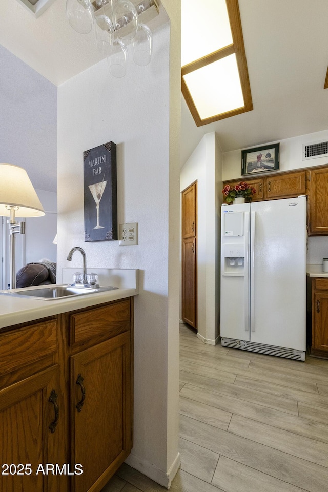 kitchen with white refrigerator with ice dispenser, sink, and light wood-type flooring