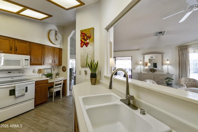 kitchen featuring sink, light wood-type flooring, white appliances, ceiling fan, and a textured ceiling