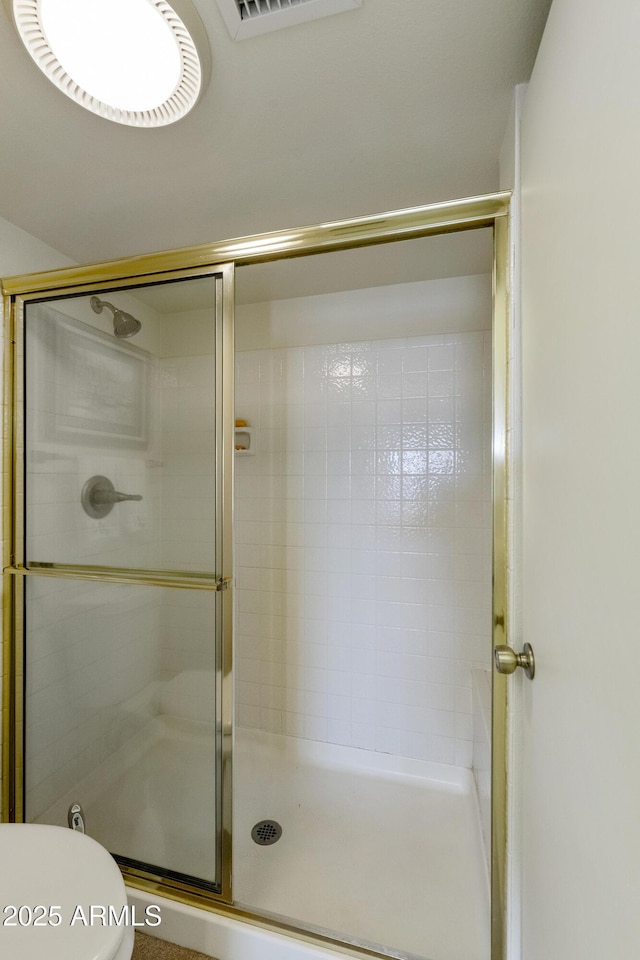 bathroom featuring a shower with door and toilet