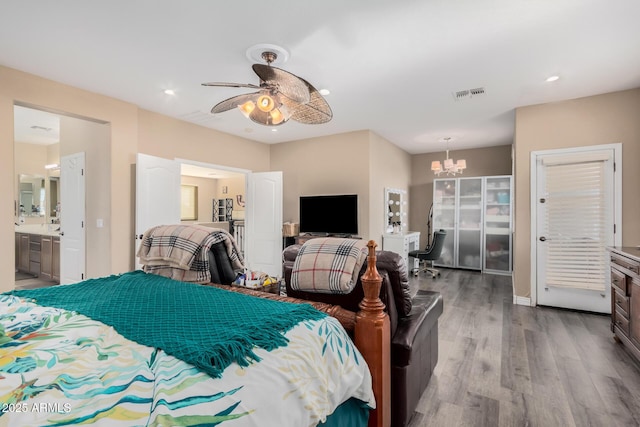 bedroom with ensuite bath, ceiling fan with notable chandelier, and wood-type flooring