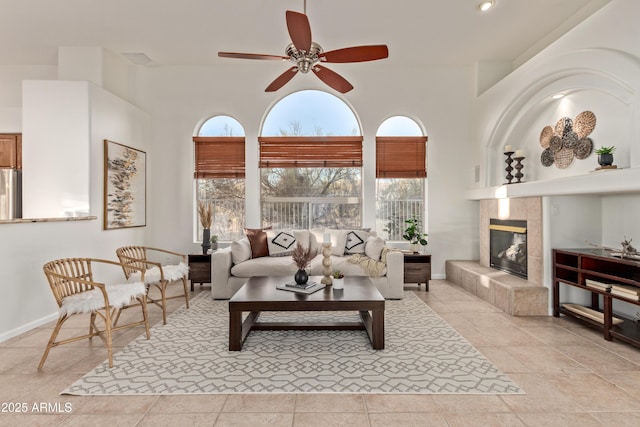 living room with a towering ceiling, a fireplace, ceiling fan, and light tile patterned floors