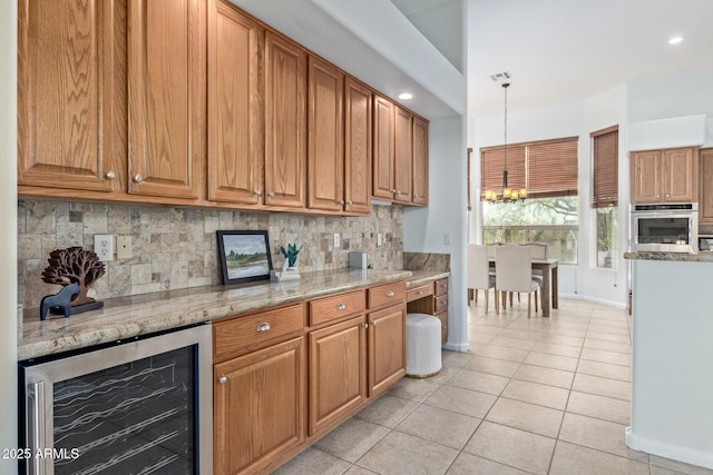 kitchen featuring light stone countertops, hanging light fixtures, oven, wine cooler, and backsplash