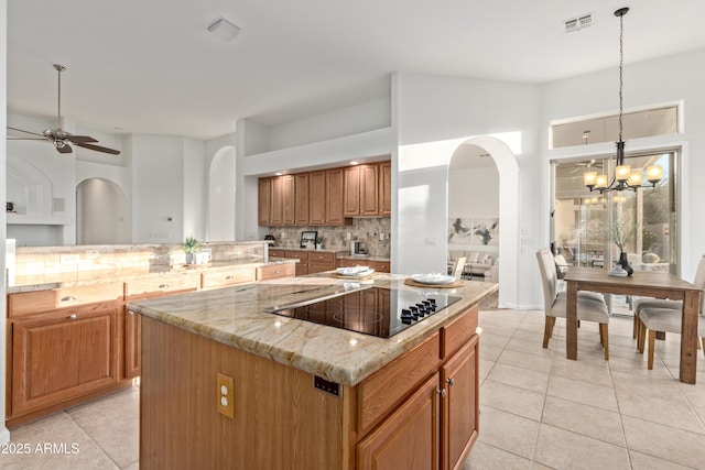 kitchen with a center island, backsplash, hanging light fixtures, light stone countertops, and black electric stovetop