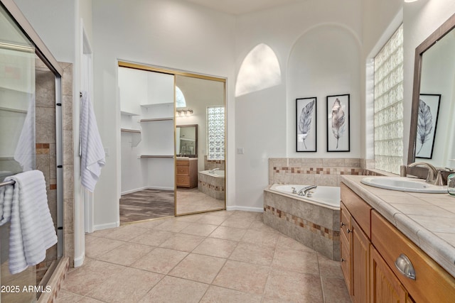 bathroom with tile patterned flooring, a relaxing tiled tub, a wealth of natural light, and vanity