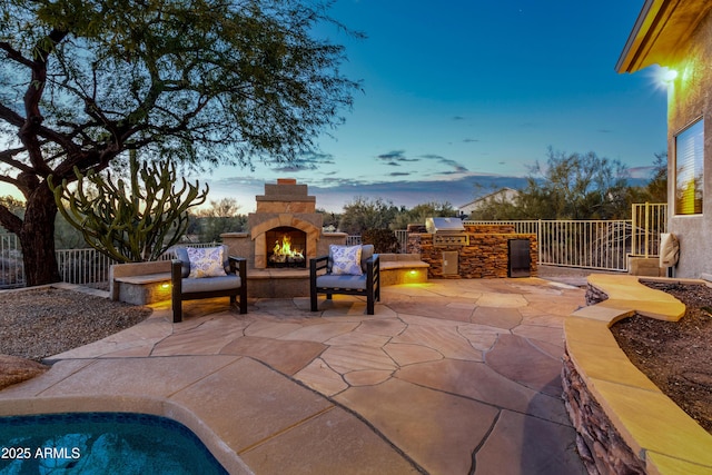 patio terrace at dusk featuring an outdoor stone fireplace, area for grilling, and a grill