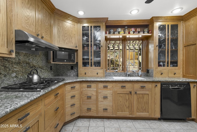 kitchen with under cabinet range hood, a sink, light stone countertops, black appliances, and tasteful backsplash