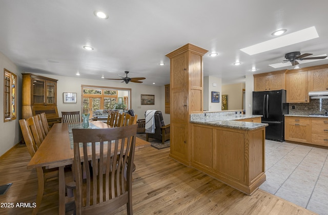 kitchen featuring a skylight, decorative backsplash, freestanding refrigerator, under cabinet range hood, and a peninsula