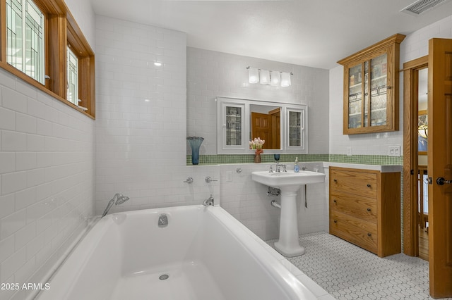 bathroom featuring a garden tub, visible vents, and tile walls