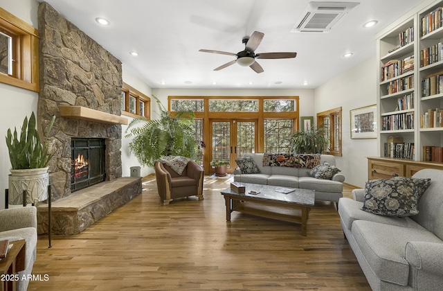 living room featuring a stone fireplace, wood finished floors, visible vents, a ceiling fan, and french doors