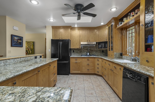 kitchen featuring under cabinet range hood, a sink, light stone countertops, black appliances, and tasteful backsplash