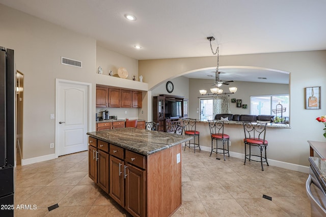 kitchen with dark stone counters, ceiling fan, light tile patterned floors, a center island, and lofted ceiling