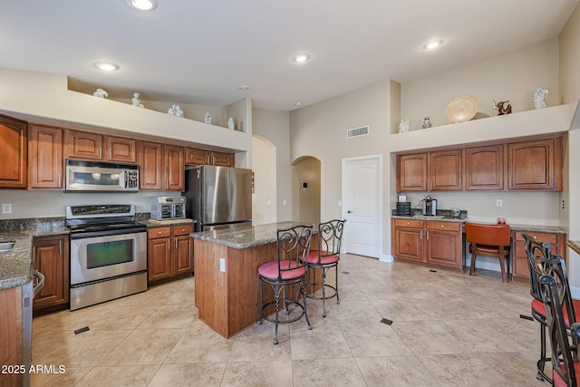 kitchen featuring a center island, dark stone countertops, a towering ceiling, and appliances with stainless steel finishes