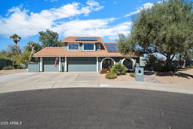 mediterranean / spanish-style house featuring concrete driveway, a tile roof, roof mounted solar panels, stucco siding, and a garage