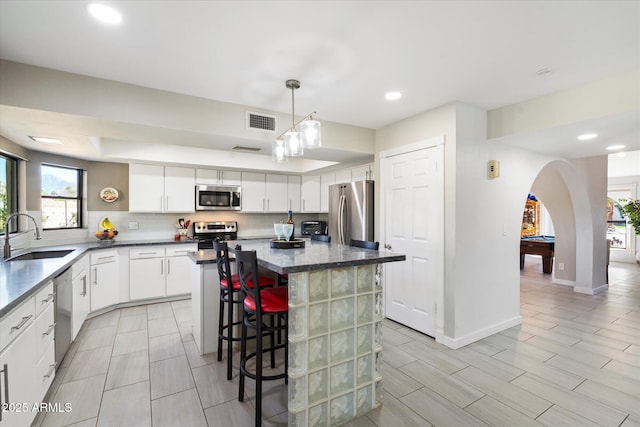 kitchen with visible vents, a kitchen island, a sink, decorative backsplash, and appliances with stainless steel finishes