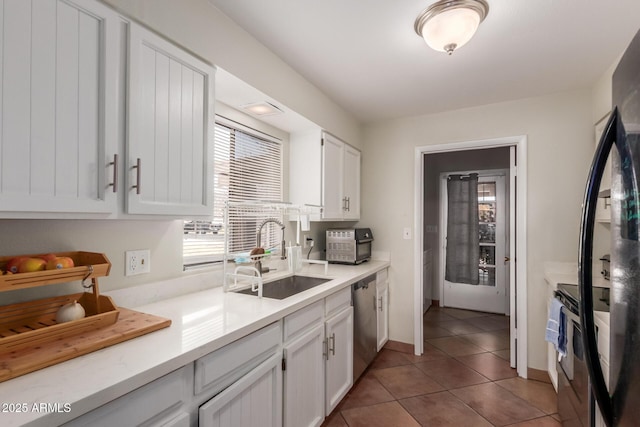 kitchen with sink, white cabinetry, black fridge, stainless steel dishwasher, and tile patterned flooring