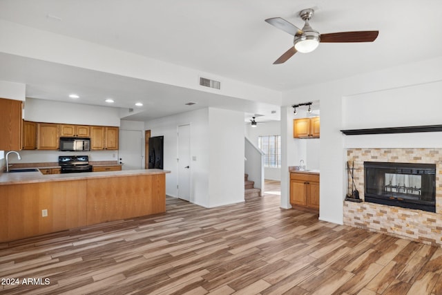 kitchen with black appliances, sink, light wood-type flooring, kitchen peninsula, and a tiled fireplace